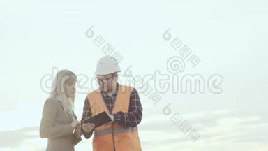 一个穿着反光背心和头盔的承包商在风车的背景下与一位商务女士进行了交易